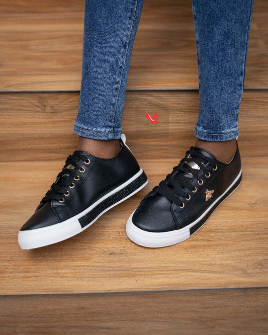 Stylish black sneakers with gold accents, perfect for casual wear, seen on a person standing on wooden floor.